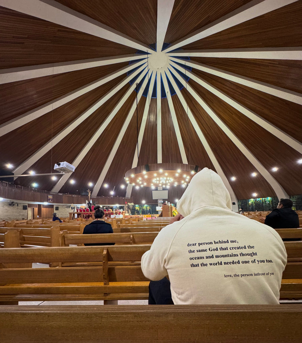 Back of a Beige BIVERSE 23' hoodie with printed text, worn inside a church.
