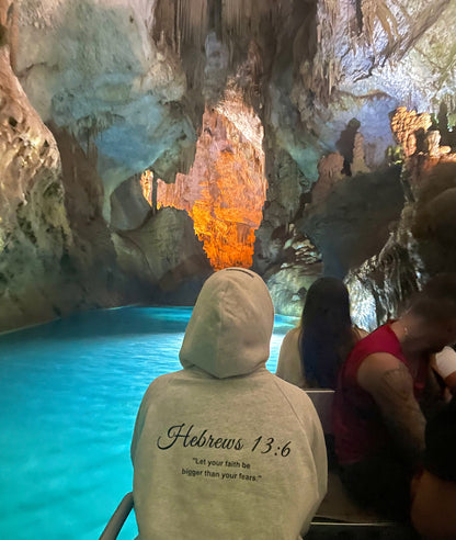 Back of a BIVERSE 23' hoodie with printed text, worn beside a grotto pool.