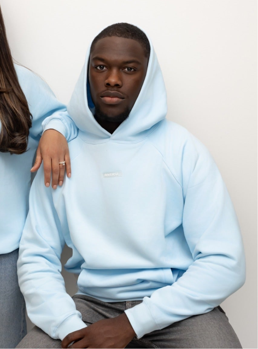 Seated model wearing the Sky blue BIVERSE hoodie with the hood up.