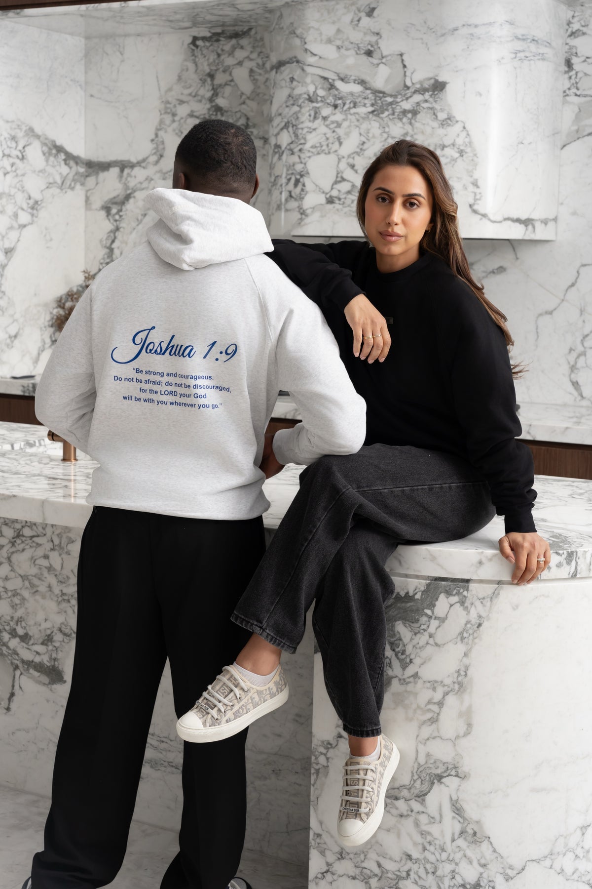 Snow white BIVERSE hoodie with a printed verse on the back beside a model in a Noir black crewneck.